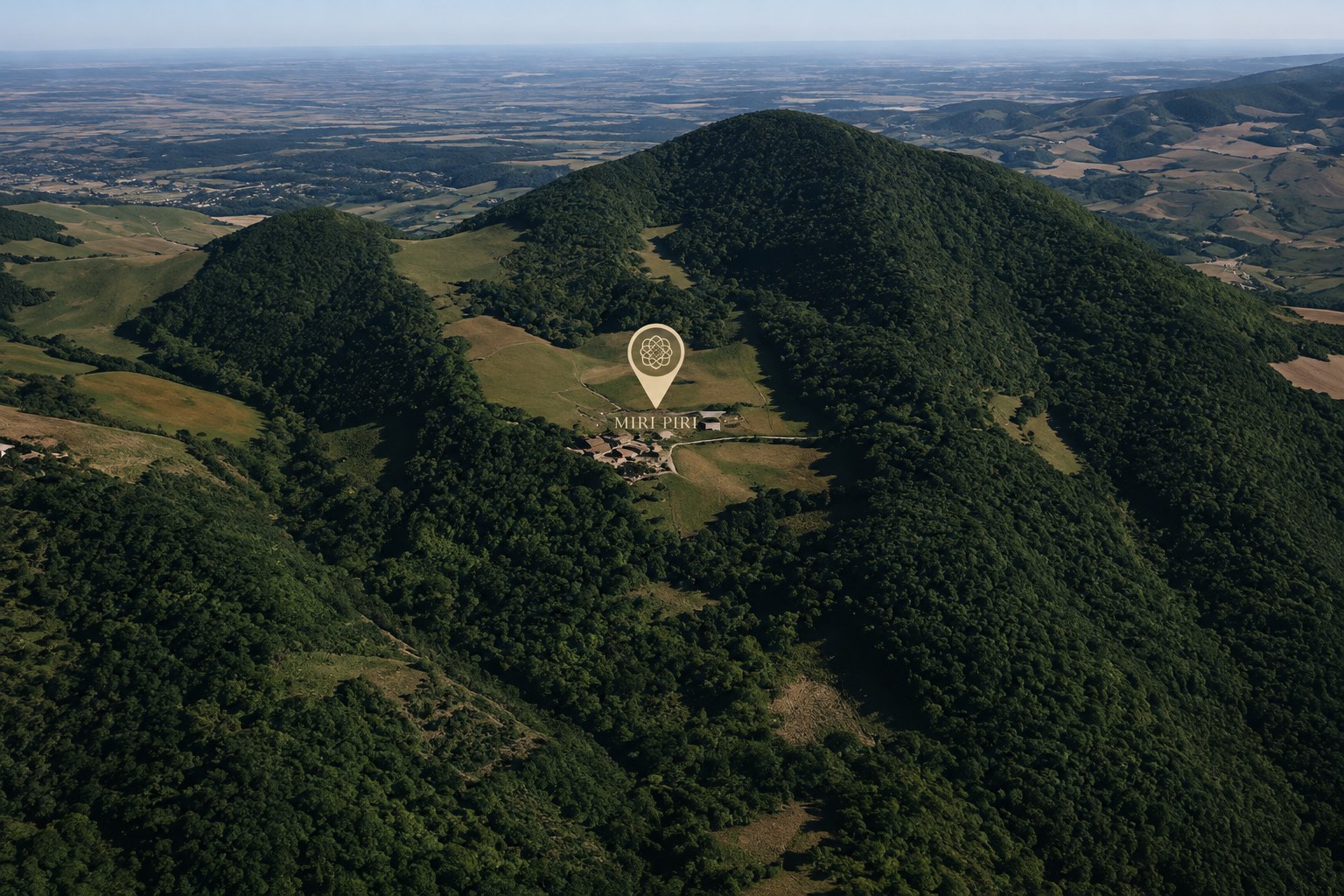 Vista dall'alto di Miri Piri: il borgo e i suoi prati, segnati da un pin, circondati dai boschi del Monte Pillerone, con i colli piacentini e la pianura all'orizzonte