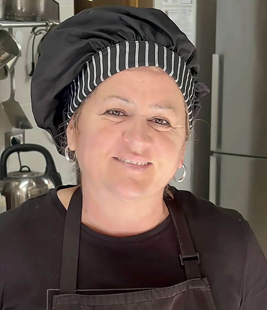 Una delle cuoche di Miri Piri, sorridente, con cappello e grembiule nella cucina della struttura
