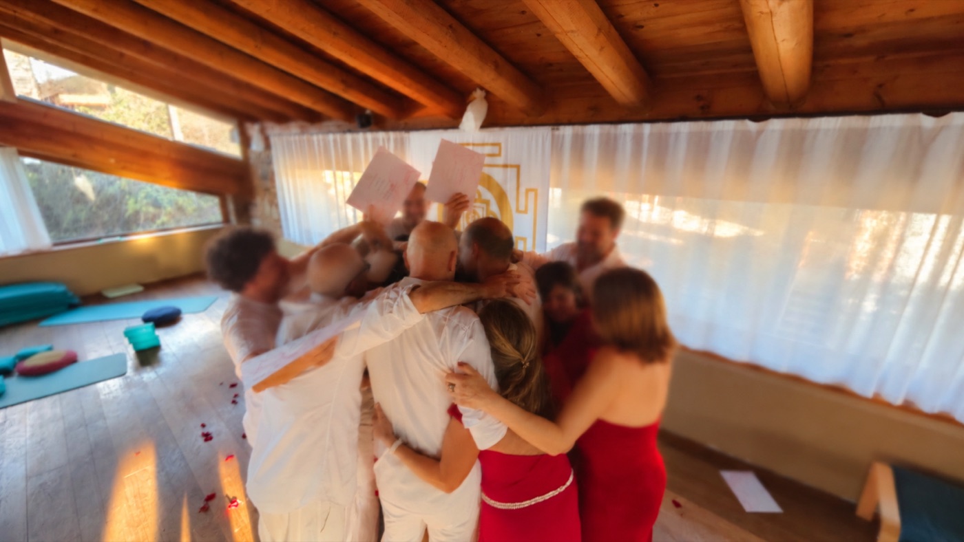 I partecipanti vestiti di bianco e di rosso si stringono in un abbraccio di gruppo alla fine di un seminario, alcuni sollevano gli attestati