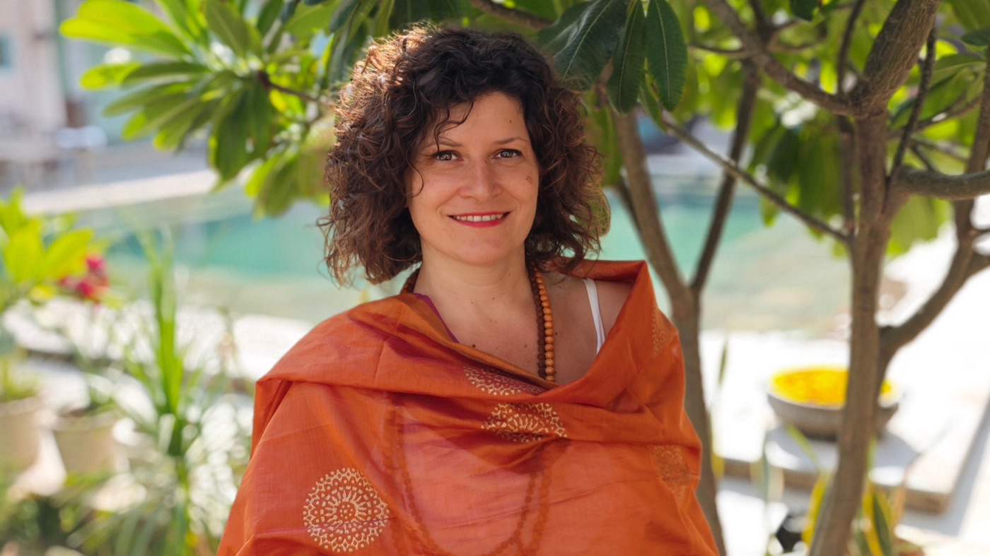 Francesca Barocci, sorridente, con uno scialle arancione e una collana di grani di legno, all'aperto fra le piante